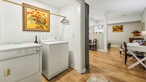 A laundry room with two white washers and dryers, a wooden floor, and a painting of flowers on the wall. - Chic 1-bedroom with WiFi and AC in fabulous Alpharetta - Blue Gate (Alpharetta)