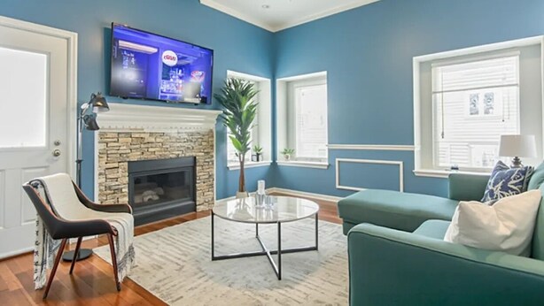 A living room with a stone fireplace, a flat-screen TV mounted above it, a green sofa, a round coffee table, and a ceiling fan.