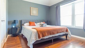 A bedroom with a bed, a nightstand, a lamp, and a window with curtains.