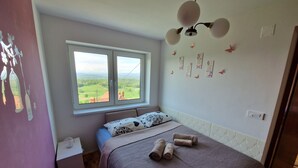 Een slaapkamer met een bed, nachtkastje, raam met uitzicht op groen en een plafondventilator.