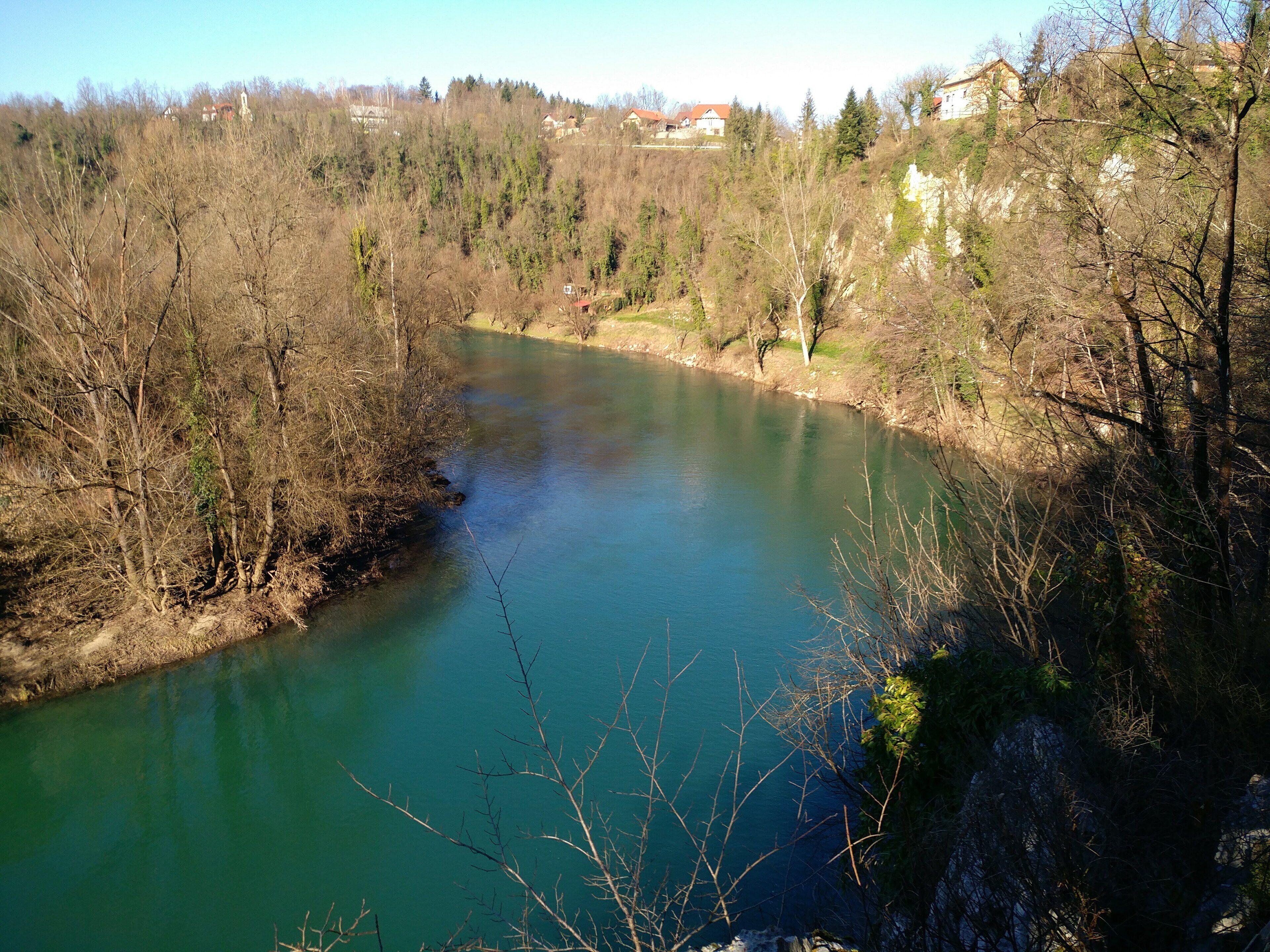 Un río rodeado de árboles y casas al fondo.