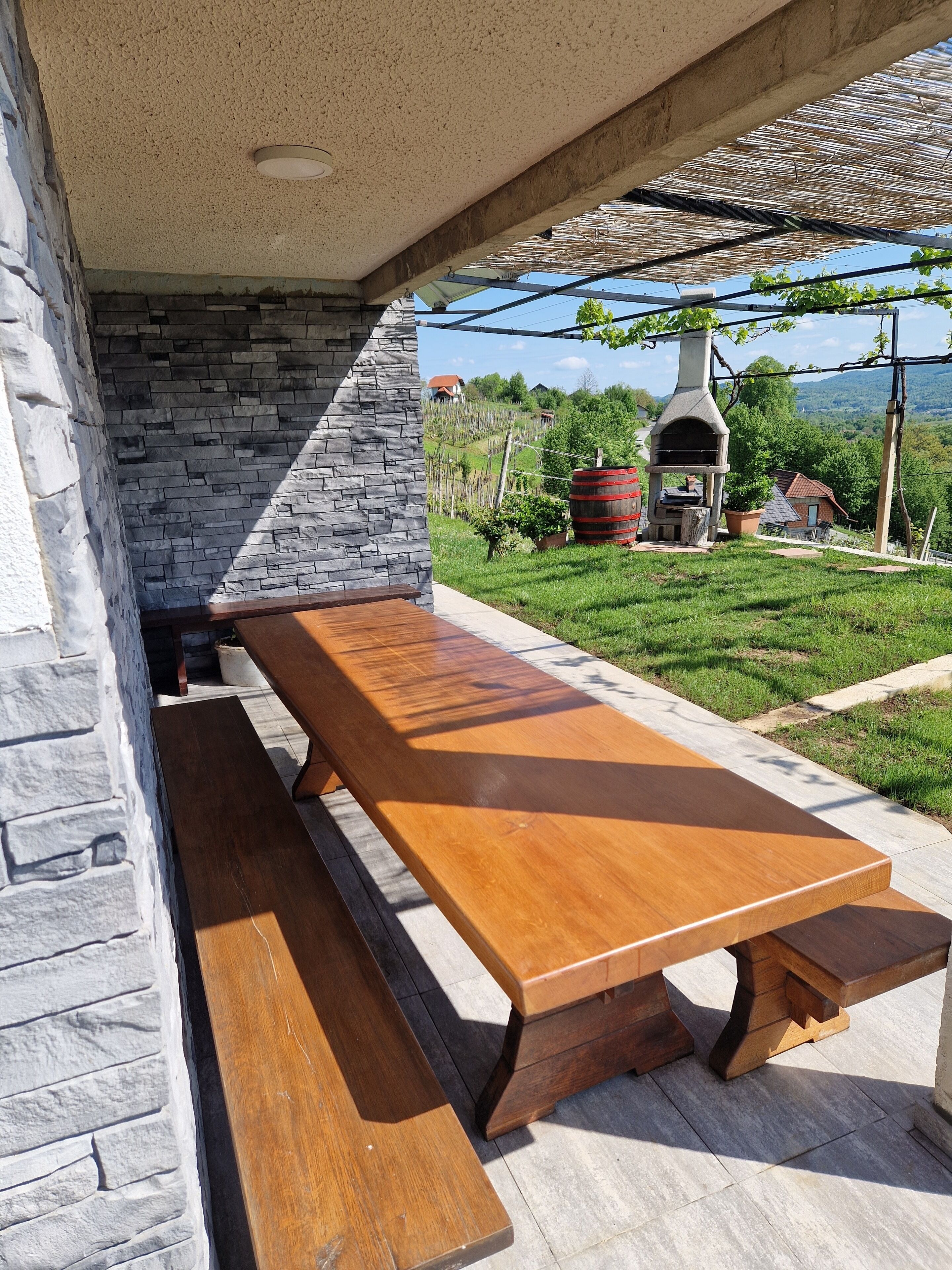 An outdoor patio with a stone wall, a wooden table, and a barbecue grill.