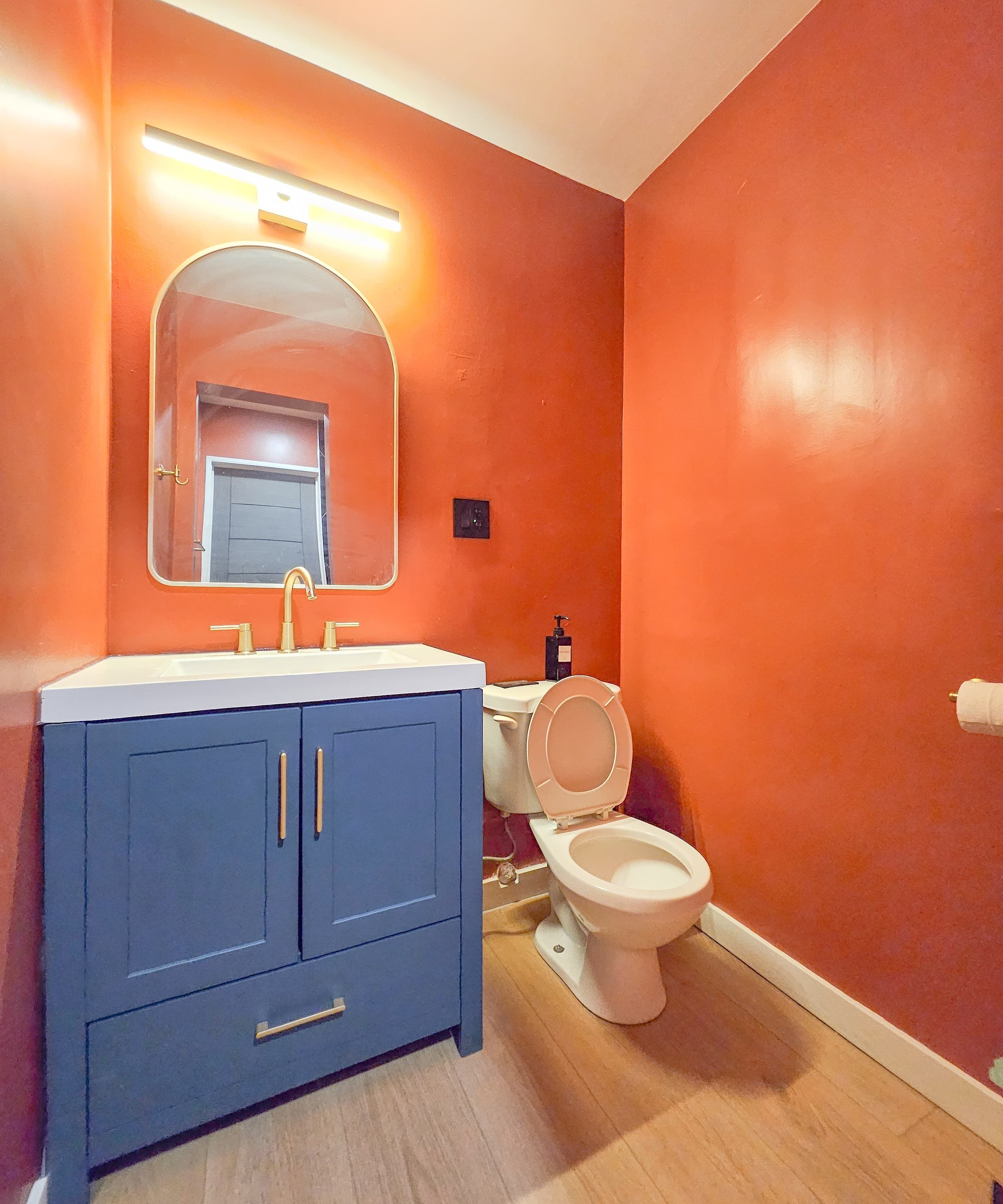 Un baño con tocador azul, inodoro blanco y paredes naranja.
