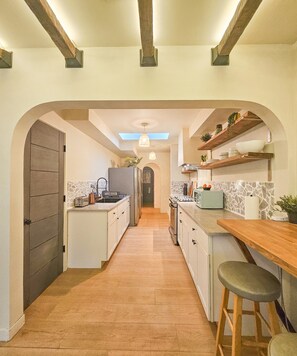 A modern kitchen with a central island, wooden beams on the ceiling, and a skylight above the sink. - Brimfield Stay (Panorama City)