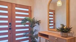 A hallway with wooden doors, a large mirror, a wooden console table, and a potted plant. - Brimfield Stay (Panorama City)