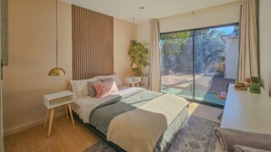 A modern bedroom with a large bed, a bedside table, a lamp, and a view of the outdoors. - Brimfield Stay (Panorama City)