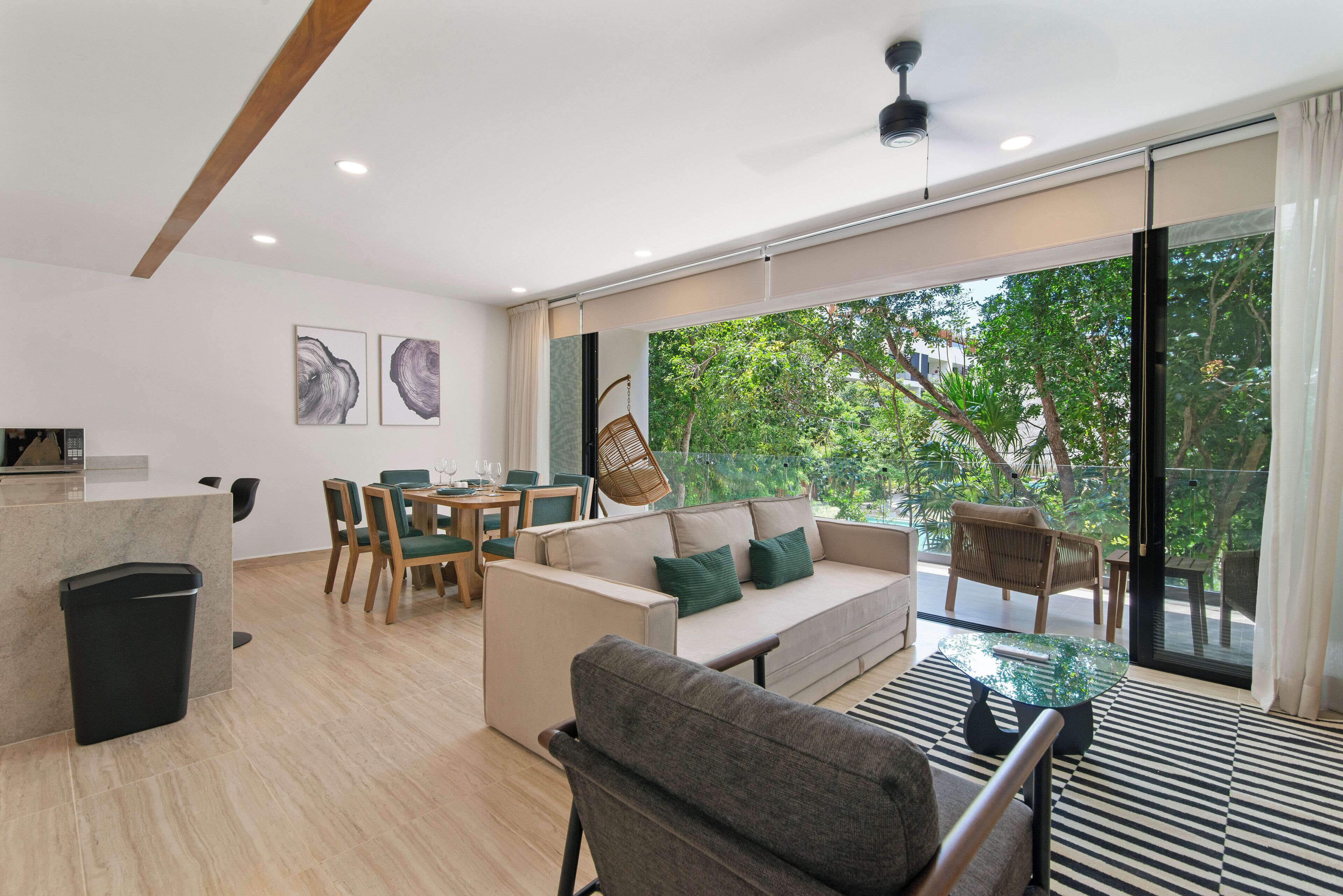 Un salon moderne comprenant un canapé, des fauteuils, une table à manger et une grande fenêtre donnant sur un paysage arboré.