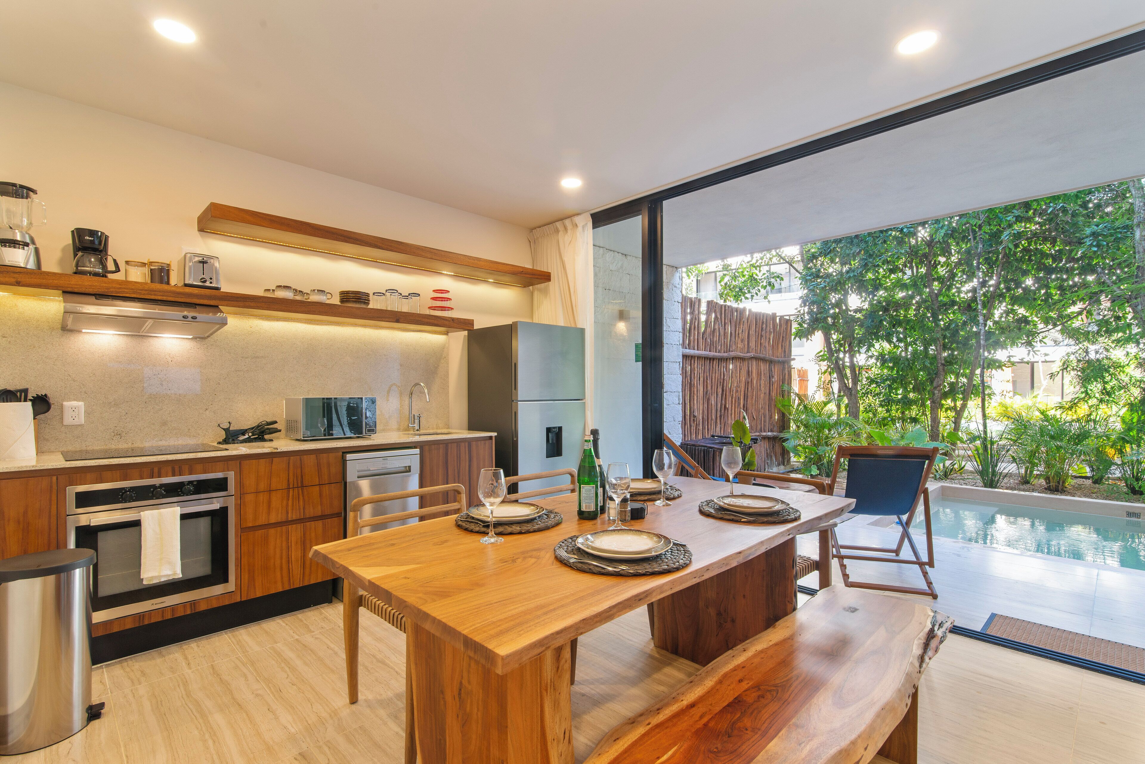A modern kitchen with wooden cabinets, a dining table set for four, and a view of a swimming pool.
