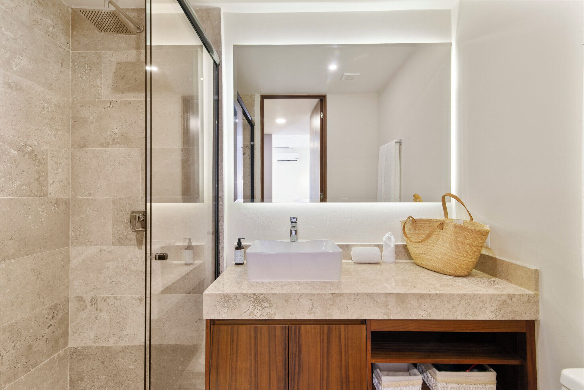 Un baño moderno con cabina de ducha de vidrio, un lavabo blanco con una pila rectangular y un mueble de tocador de madera.