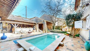 A swimming pool with a stone border, a wooden deck, and a stone building with a tiled roof. - Nice home in Saint-Simon with private swimming pool, can be inside or outside (Saint-Simon)