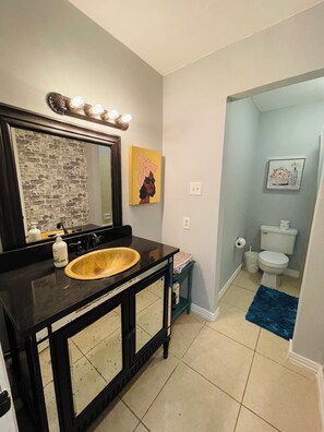 Clean and functional bathroom with a large mirror, wooden bowl sink, and framed artworks.