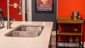 A kitchen with a modern sink, a metal faucet, a wooden shelf with glasses, and a poster on the wall. - 2 Bedroom Buckhead Suite (Atlanta)