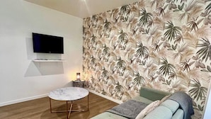 A modern living room with a sofa, a small round table, and a flat-screen TV mounted on the wall.