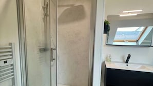 A modern bathroom with a glass-enclosed shower, a white vanity with a mirror, and a view of the sky through the window.