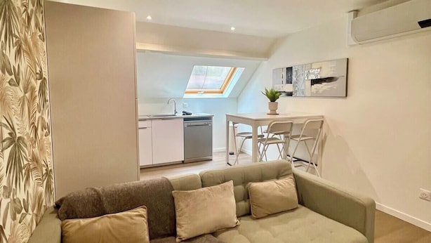 A modern living room with a sofa, a dining table with chairs, a kitchen area, and a skylight.