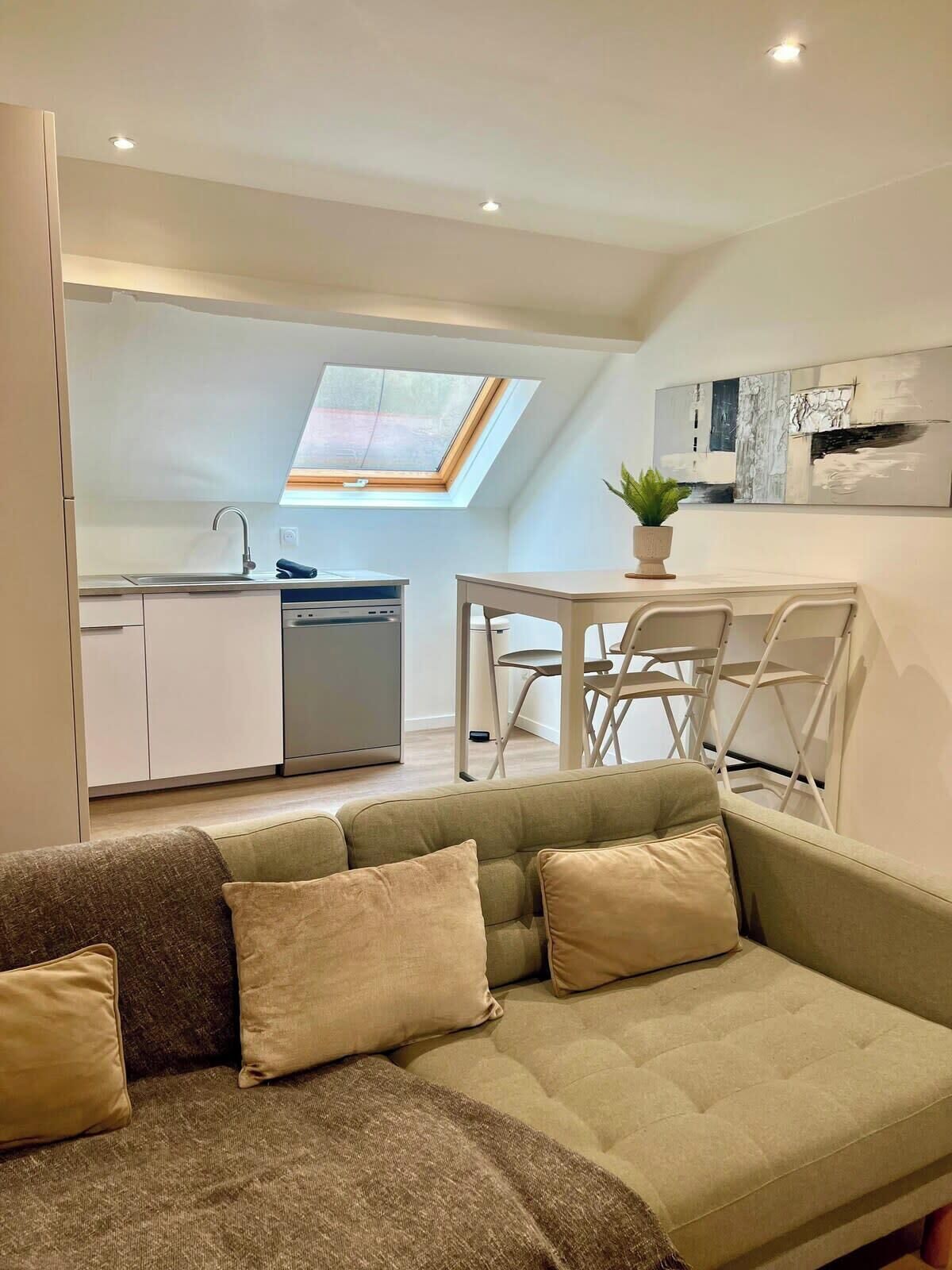 Un appartement moderne de style « loft », comprenant un coin repas, une kitchenette et un espace de vie confortable avec un canapé et des coussins.
