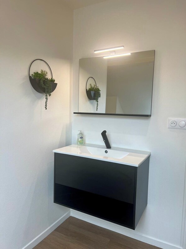 A modern bathroom with a white sink, black cabinet, and two wall-mounted plant holders.