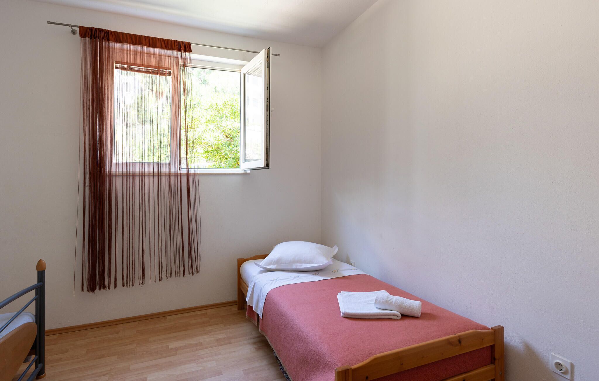 Une petite chambre avec un lit simple, une tête de lit en bois, une fenêtre avec des rideaux et un plancher en bois.