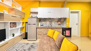 A compact living space with a kitchenette, a sofa with yellow cushions, and a TV on a wooden cabinet. - BSB Apartment  (Tirana)