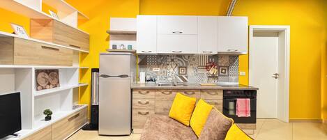 A compact living space with a kitchenette, a sofa with yellow cushions, and a TV on a wooden cabinet.