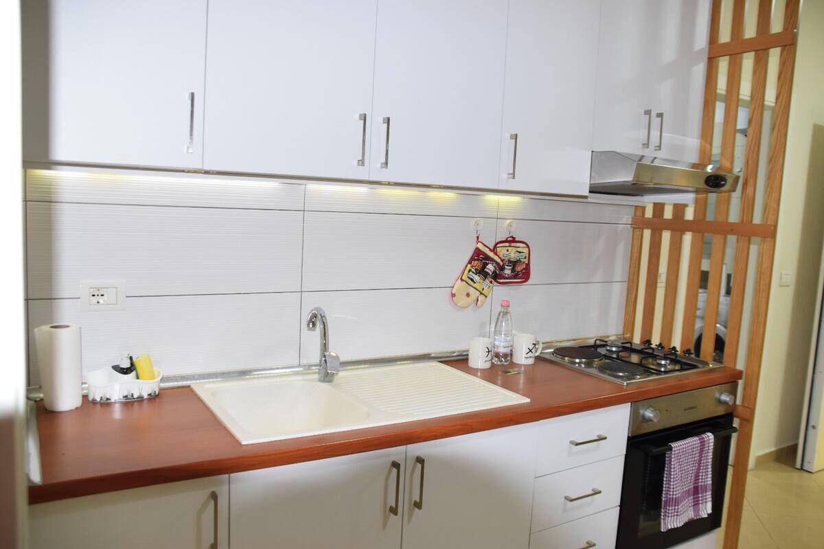 Una cocina con armarios blancos, encimera de madera, pileta de acero inoxidable y estufa.