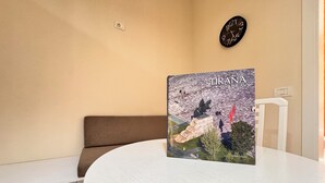 A round table with a book titled "TIRANA from the Air" on it, a brown sofa, a white chair, a wall clock, and a light switch. - BSB Apartment  (Tirana)