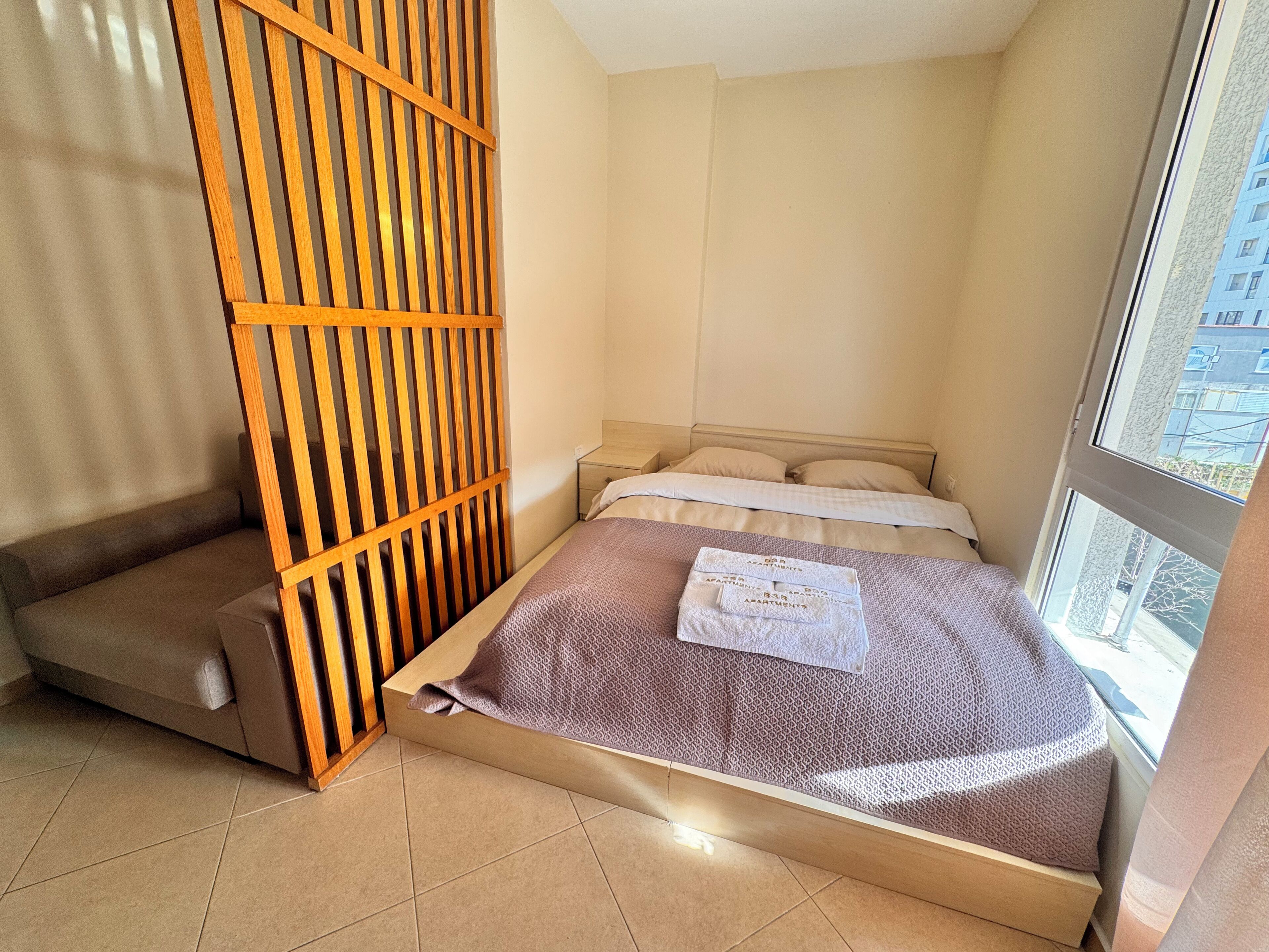 Une chambre d’hôtel compacte comprenant un lit, un petit coin salon, une fenêtre avec vue et une cloison en bois.