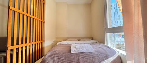A small, modern bedroom with a bed, a wooden partition, and a window with a city view.