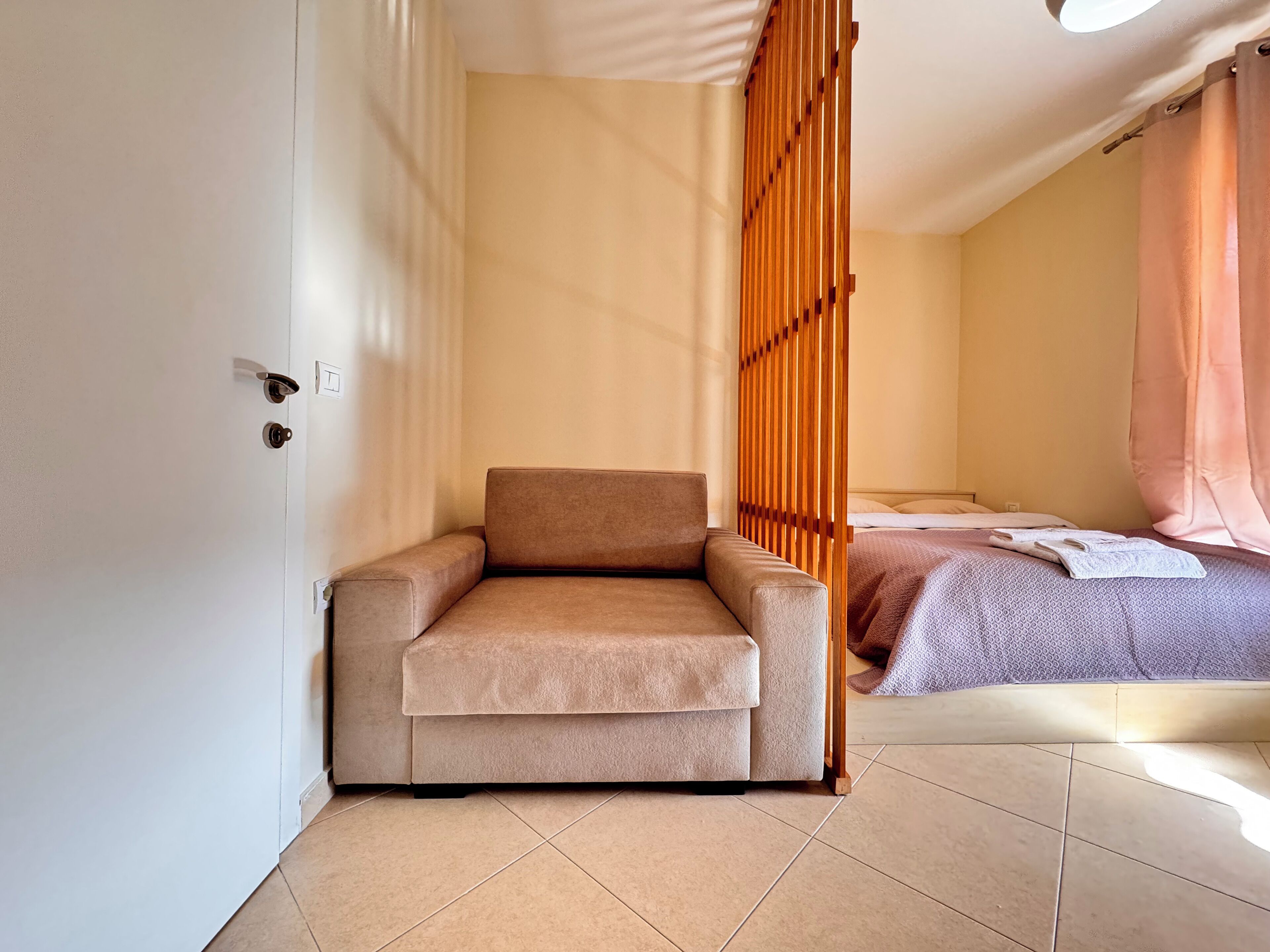 Et værelse med en beige sofa, en seng med et mønstret sengetæppe og en trævæg.