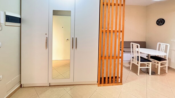 A room with a white wardrobe, a wooden partition, a dining table with chairs, and a clock on the wall. - BSB Apartment  (Tirana)