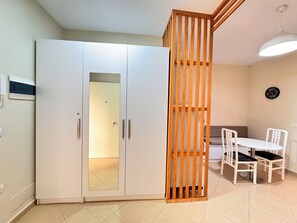 A room with a white wardrobe, a wooden partition, a dining table with chairs, and a clock on the wall. - BSB Apartment  (Tirana)
