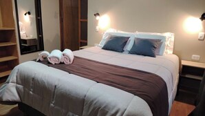 A neatly made bed with a brown and white duvet, two pillows, and rolled towels on the side. There are two bedside lamps and a mirror on the wall. - Hotel Golden Killa (Huaraz)