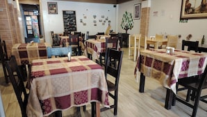 A dining area with tables covered in patterned tablecloths, wooden chairs, and a brick wall with framed photos. - Hotel Golden Killa (Huaraz)