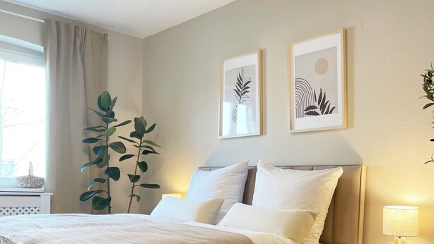 Een keurig opgemaakt slaapkamer met een bed, nachtkastjes, een lamp en twee decoratieve wandschilderingen.