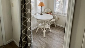 Une pièce avec une table ronde blanche, deux chaises en osier, une lampe et des rideaux à motifs.