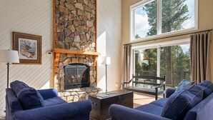 Una sala de estar con chimenea de piedra, sofás azules y un ventanal con vista a una terraza.
