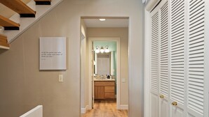 Un pasillo con suelo de madera, una puerta blanca con picaporte dorado y una cita enmarcada en la pared.