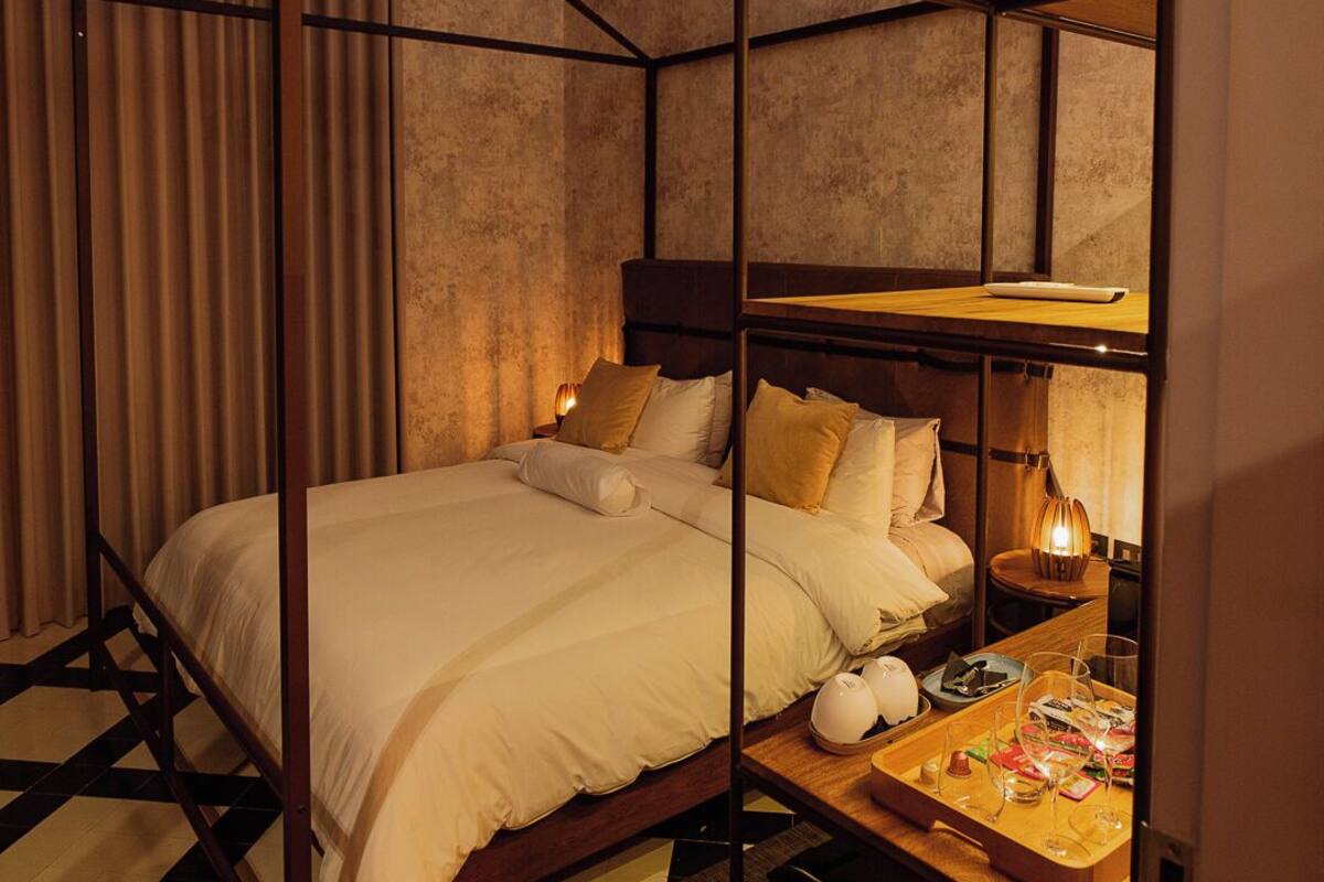 A room with a bed, a wooden nightstand, and a small table with a lamp.
