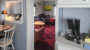 Un espace de vie compact comprenant un coin cuisine, un coin repas avec une table et des chaises, un canapé et une machine à café.