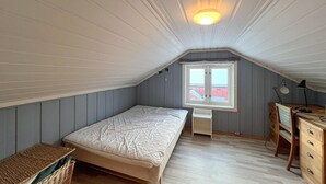Une petite chambre avec un lit simple, un plafond en pente, une fenêtre donnant sur un beau paysage, un bureau avec une lampe et une chaise.