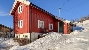 Une maison en bois rouge avec une porte verte, un petit porche et une allée enneigée.