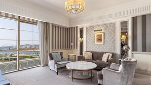 A spacious room with a large window offering a city view, a round coffee table, and a grey sofa with multiple cushions.