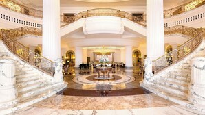 A grand lobby with marble floors, ornate golden railings, and a central chandelier.