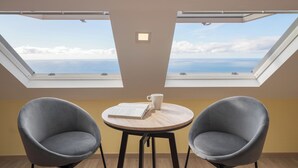 Una habitación con dos tragaluces, una mesa redonda de madera, dos sillones grises y una taza blanca sobre la mesa.