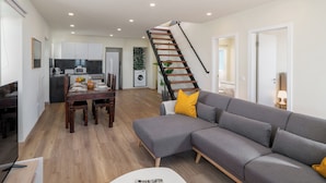 Una sala de estar moderna con un sofá gris, una mesa de comedor de madera y una escalera que conduce a un nivel superior.