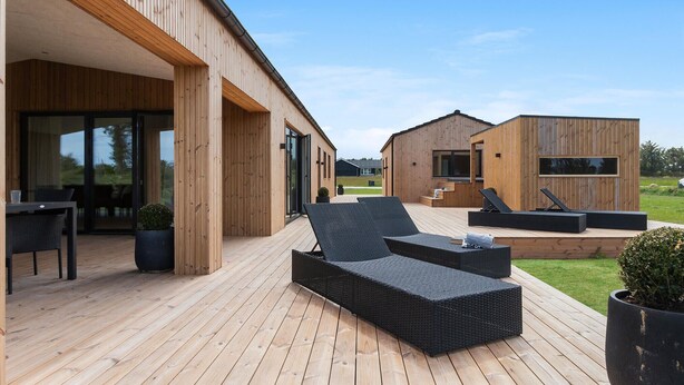 Ett modernt trähus med en veranda, utomhusmöbler och en liten trädgård.