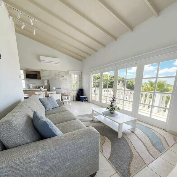 A spacious living area with a large sofa, a coffee table, and a view of the outdoors through large windows.