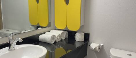 A bathroom with a white sink, mirror, and toilet. There are yellow cabinets above the sink and a black countertop.