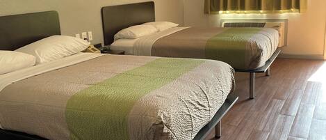 A hotel room with two single beds, a window with curtains, a heater, and a wooden floor.