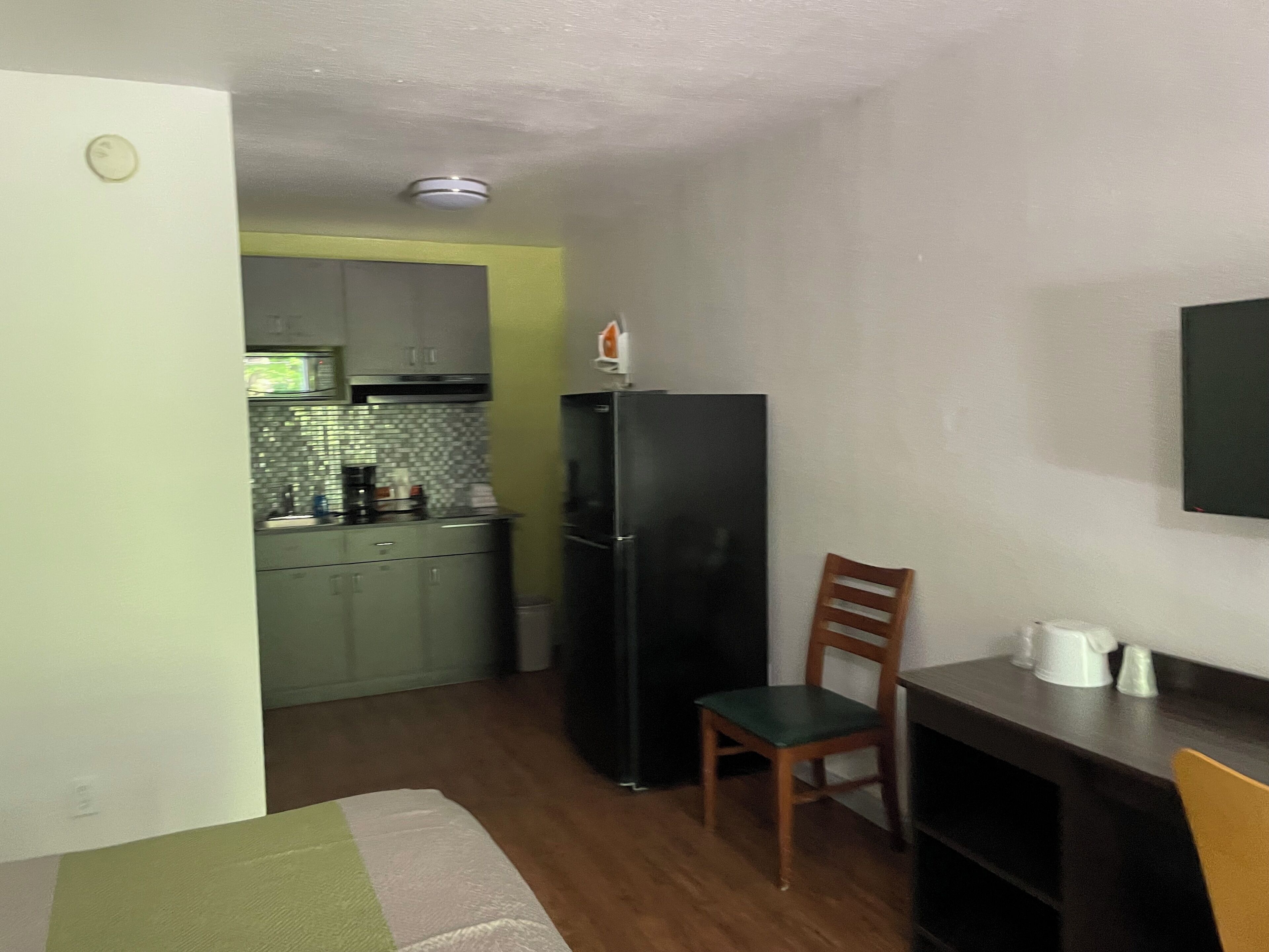 Una cocina compacta con refrigerador, microondas y pileta. Hay una silla de madera y una mesa pequeña con una jarrón blanco.